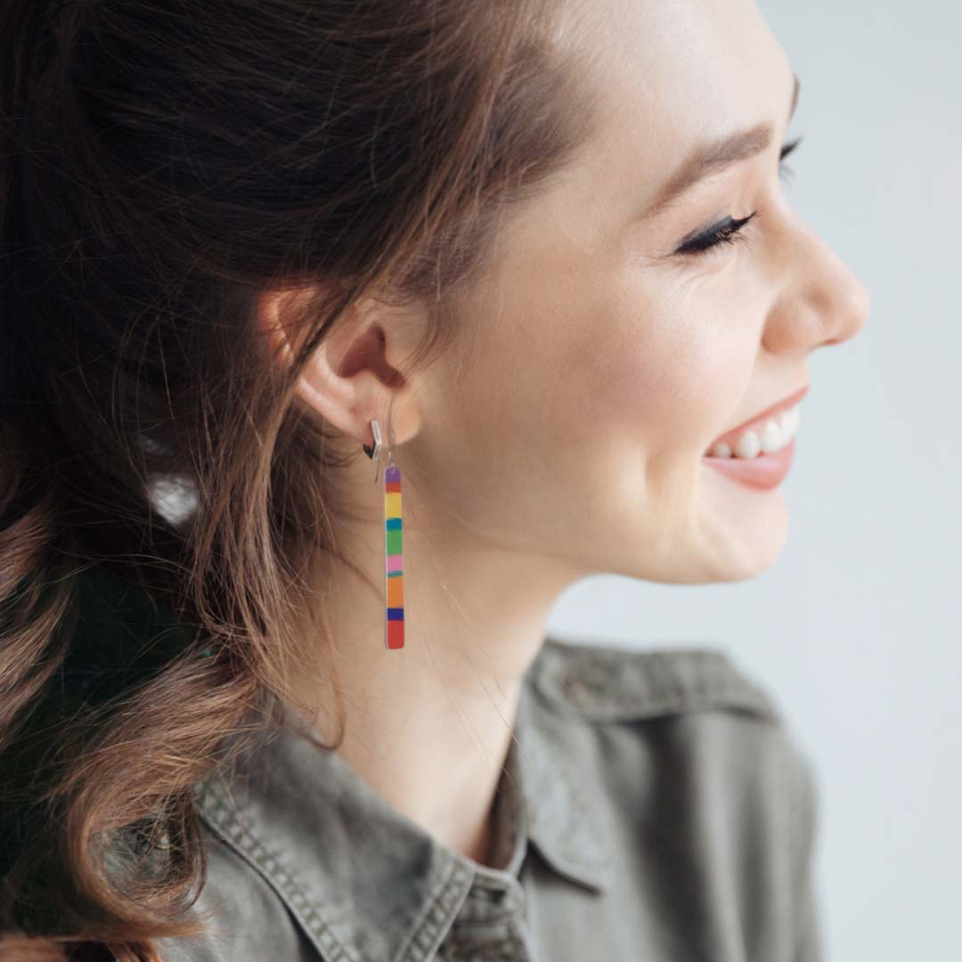 Young woman wearing long variegated rainbow  dangle earrings in a color block design by ColorUpLife.