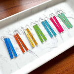 Colorful polka dot earrings sitting on a white tray with a wooden surface underneath.