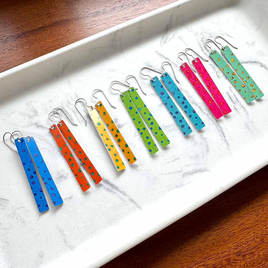 Colorful polka dot earrings sitting on a white tray with a wooden surface underneath.