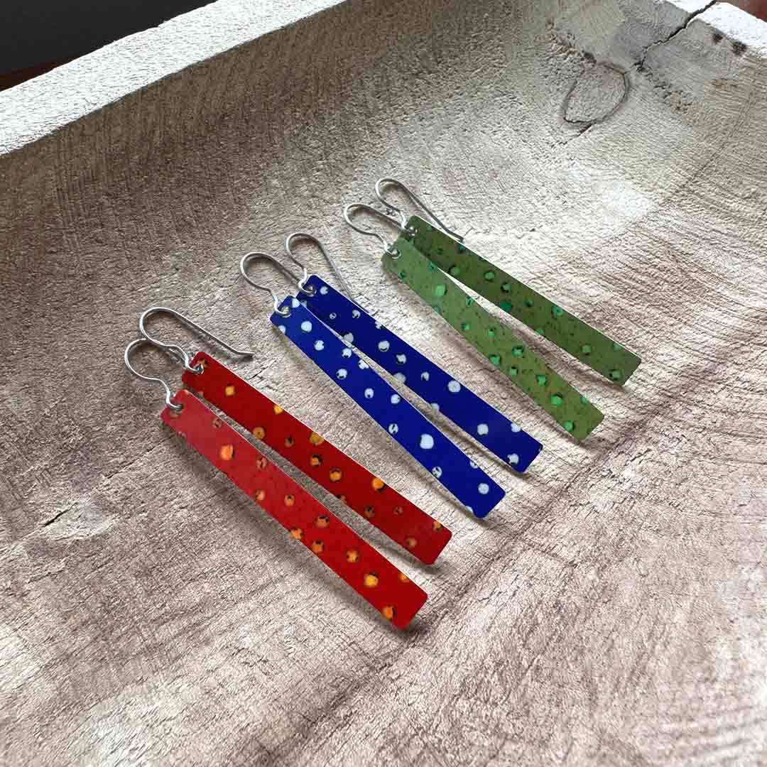 Colorful dangle earrings with polka dot designs in fall colors, sitting on a wooden surface.