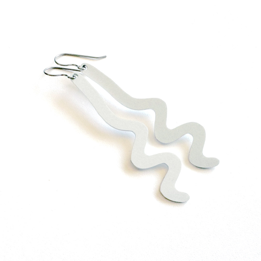 A pair of minimalist, wavy, light gray dangle earrings made of aluminum metal with silver-toned titanium fishhook ear wires, displayed on a clean white background.