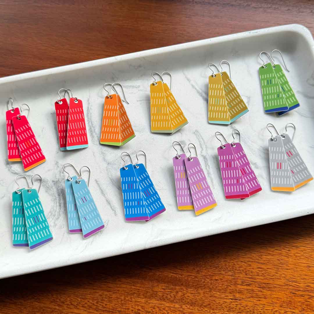 Colorful geometric earrings displayed on a white tray with a wooden surface underneath by ColorUpLife.