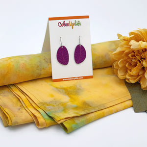 A pair of plum colored small leaf earrings displayed on a sunny yellow rayon scarf by ColorUpLife.