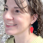 A close-up of a woman wearing a bright red vintage light bulb dangle earring for Christmas, shown against a sparkly silver background.