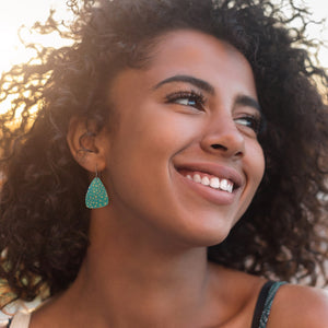 A teen girl wearing a pair of small triangular dangles earrings in seafoam green with polka dots by ColorUpLife