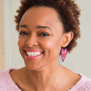 A woman wearing a pair of pink and purple heart dangle earrings by ColorUpLife.